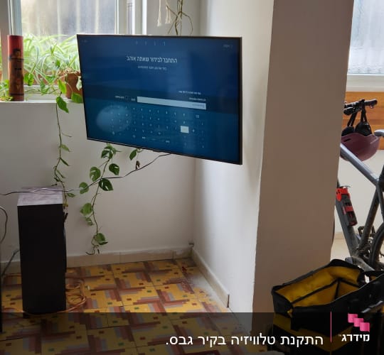 תיק כלים צהוב ושחור ליד טלוויזיה תלויה על הקיר